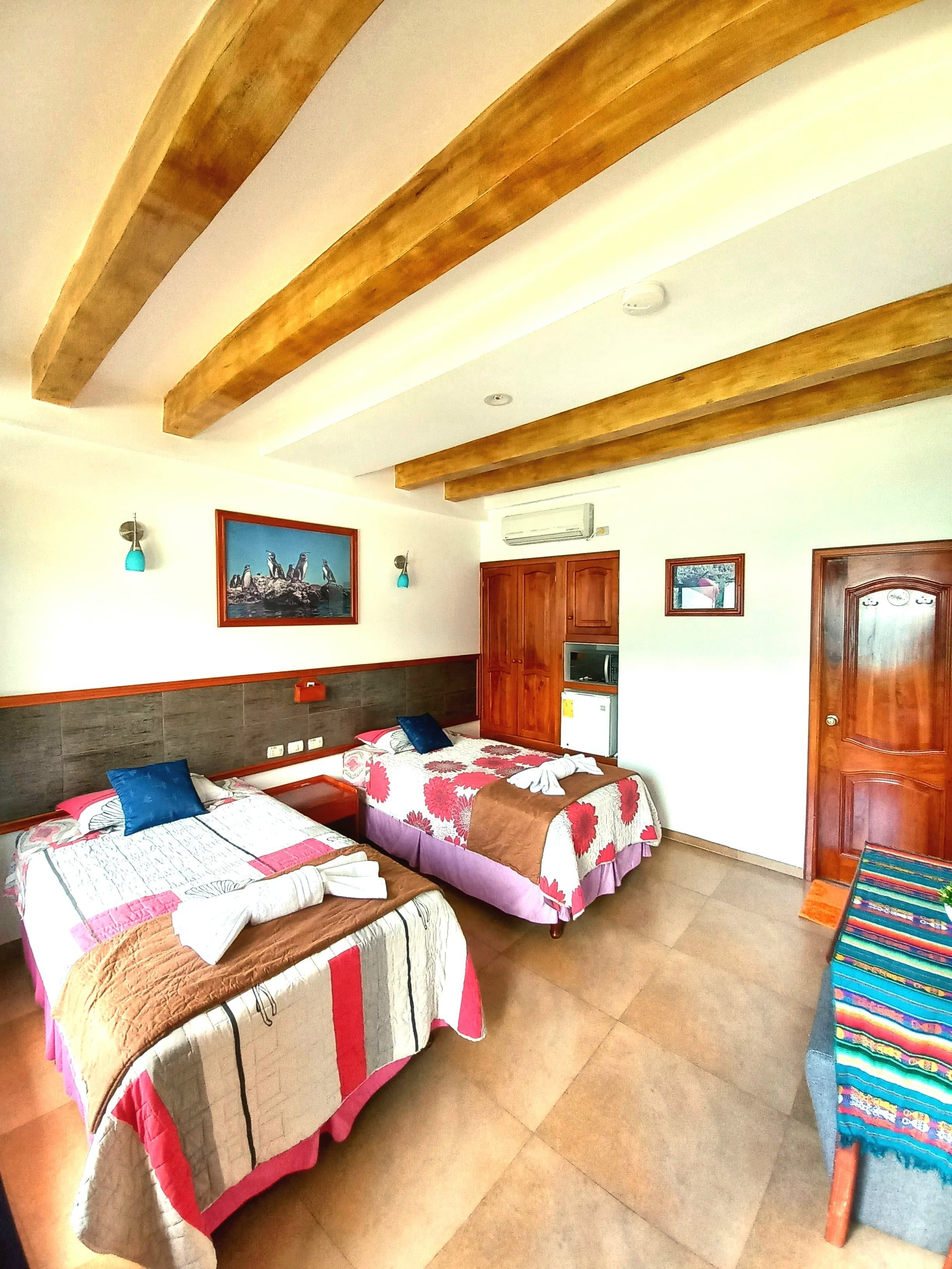 A room with two beds, wooden beams on the ceiling, a wall-mounted air conditioner, and a door with a small window.