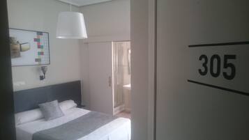 Una habitación de hotel con una cama, una lámpara blanca, una obra de arte en la pared y una puerta con el número 305.