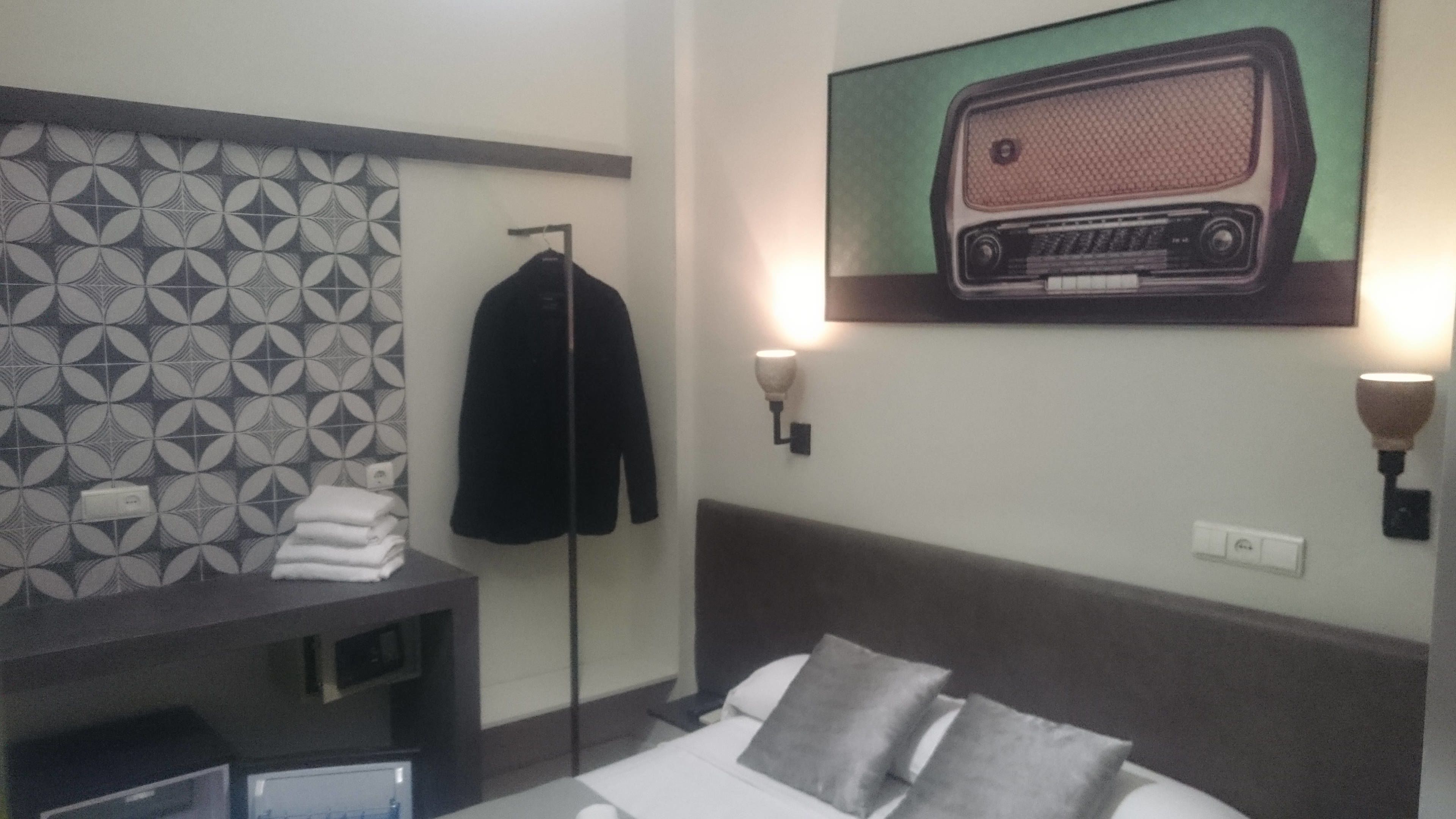 Una habitación de hotel con una cama, un televisor de pared, un perchero y un papel tapiz estampado.