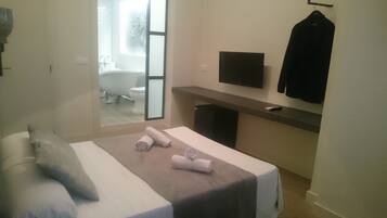 Un dormitorio moderno con cama, televisor montado en la pared y vista al baño.