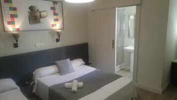 Ein Hotelzimmer mit Bett, Kopfteil, Wandleuchte und einem durchgegangene Tür sichtbaren Badezimmer.