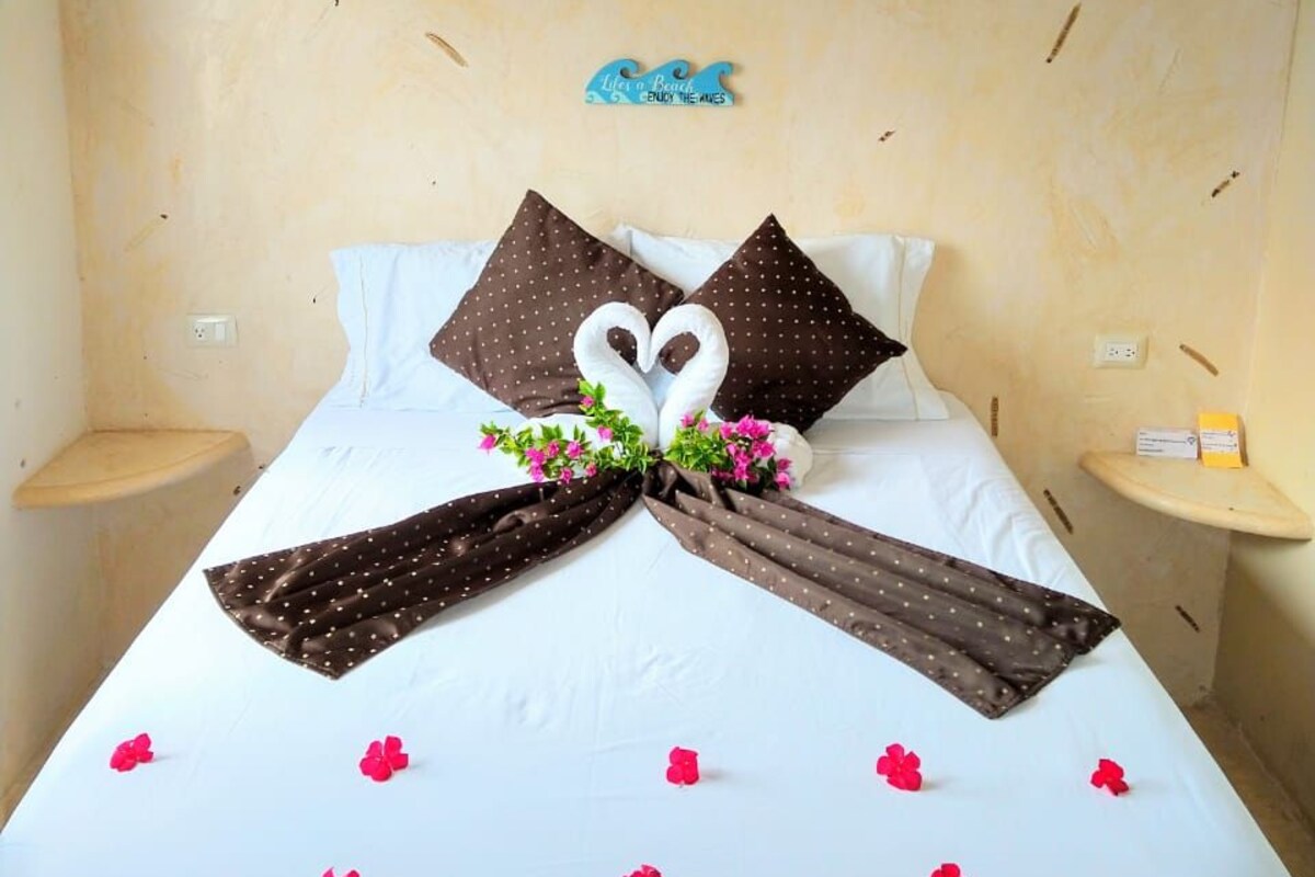 Una cama bien hecha con un arreglo de almohadas en forma de corazón, una mesita de noche pequeña y una decoración en la pared.