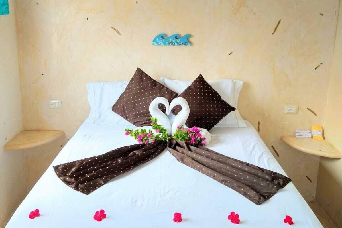 A neatly made bed with a heart-shaped pillow arrangement, a small bedside table, and a wall decoration.