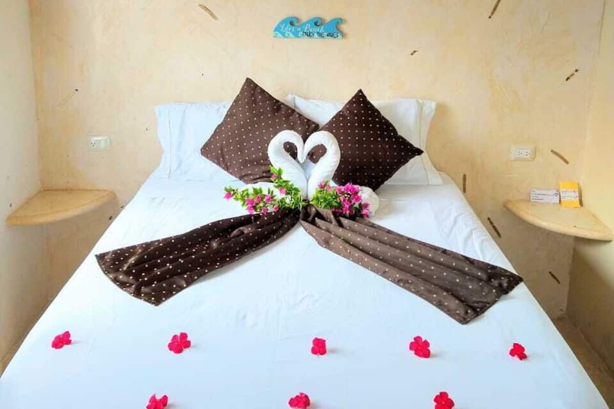 Una cama bien hecha con un arreglo de almohadas en forma de corazón, una mesita de noche pequeña y una decoración en la pared.