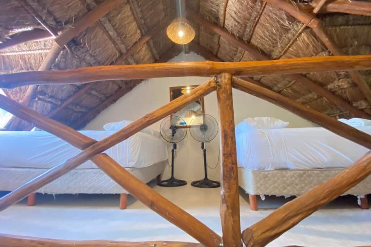 A room with a wooden ceiling structure, two beds, and two standing fans.