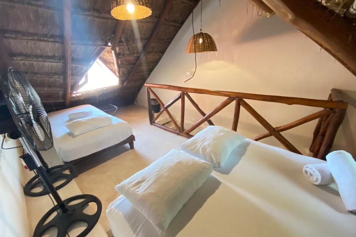 Acogedor cuarto en ático con dos camas, un ventilador y una lámpara de techo tejida.