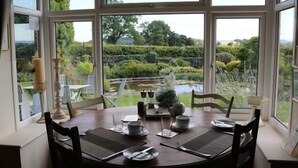A dining area with a table set for two, large windows with a view of a garden and pond, and a candle on the table. - Mortimer Trail B & B (Leominster)