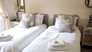 A hotel room with two beds, each with white linens and decorative pillows. There is a nightstand with a lamp and a small table with a decorative item. - Mortimer Trail B & B (Leominster)