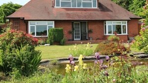 A two-story house with a brick exterior, large windows, and a garden with a pond and flowers. - Mortimer Trail B & B (Leominster)