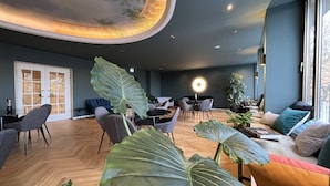 A modern interior with a large plant in the foreground, a dining area with chairs and tables, and a ceiling with a circular design. - Hotel Rotkreuzplatz (Munich)