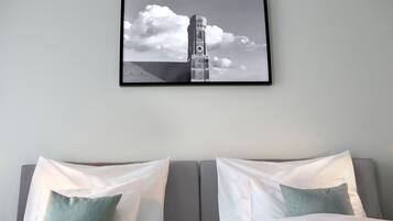 A hotel room with a bed, two pillows, and a framed picture of a tower on the wall.