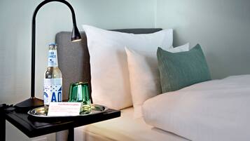 A hotel room with a bed, pillows, a nightstand with a bottle, glasses, and a tray with a menu.