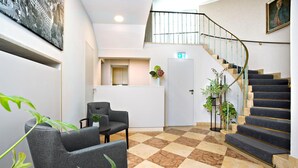 A lobby with a checkered floor, a staircase, and seating area. - Hotel Rotkreuzplatz (Munich)