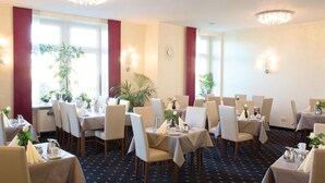 A dining area with tables set for service, chairs, and potted plants.