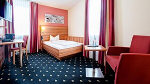 A hotel room with a bed, a desk, a chair, and a small table.