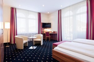 Een hotelkamer met een bed, een bureau met stoel, een televisie en een lamp.