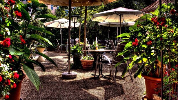 An outdoor patio with tables and chairs, surrounded by potted plants and umbrellas. - Hotel Alter Telegraf (Graz)