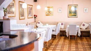 A restaurant with hexagonal tiled flooring, white tablecloths, and a variety of framed artworks on the walls. - Hotel Alter Telegraf (Graz)