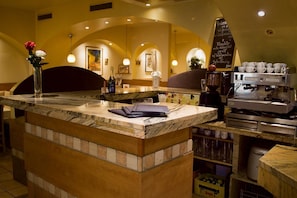 Un espace bar doté d’un comptoir en marbre, d’une machine à café et d’un tableau noir servant de menu.