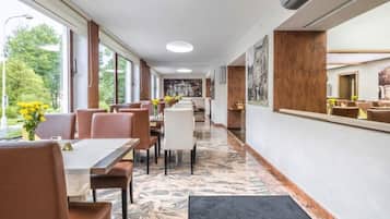 Un espace de restauration d’hôtel avec des tables et des chaises, de grandes fenêtres et un sol en marbre.
