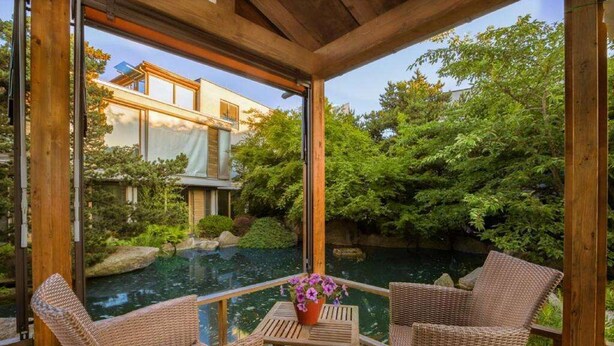 A wooden deck with wicker chairs and a table, overlooking a koi pond and lush greenery. - Hotel Schindlerhof (Nuremberg)