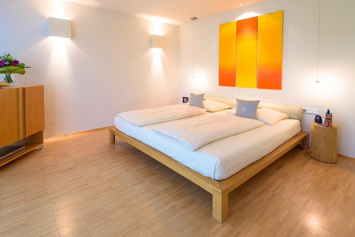 Un dormitorio moderno con una cama de madera, mesitas de noche y una lámpara fijada a la pared.