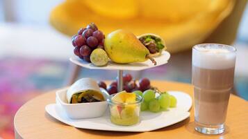 Una bandeja de tres niveles con frutas y postres sobre una mesa redonda, junto a un vaso de leche.