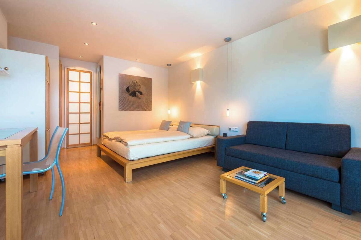A modern bedroom with a bed, a sofa, a desk, and a chair.