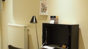 A compact office space with a desk, chair, radiator, and a wall calendar. - Hotel Schindlerhof (Nuremberg)