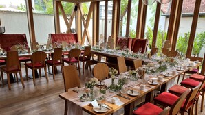 A long dining table set with red upholstered chairs, white tablecloths, and floral centerpieces. - Hotel Schindlerhof (Nuremberg)