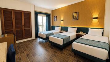 Habitació d'hotel amb tres llits, terres de fusta, una escriptori i vista per una porta.