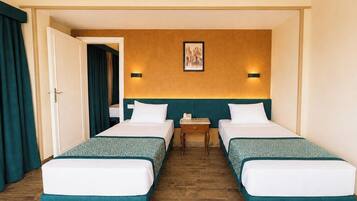 Camera d'albergo con due letti singoli, pavimento in legno, una porta con tende e un quadro appeso al muro.