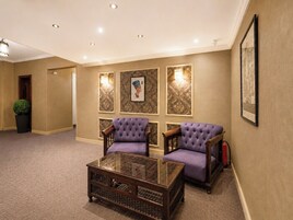 A hotel lobby with two purple armchairs, a glass coffee table, and decorative wall panels.