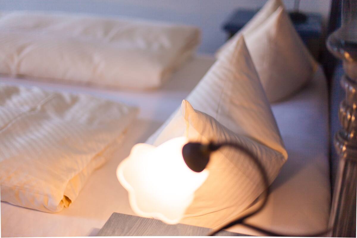 Neatly folded white linens on a bed with a small, lit candle in a cone-shaped holder.