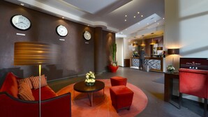 A lobby with a red sofa, a round table, and two clocks on the wall. - Hôtel de Berny (Antony)