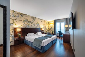 A hotel room with two beds, a desk, a chair, a TV, and a window with curtains. - Hôtel de Berny (Antony)