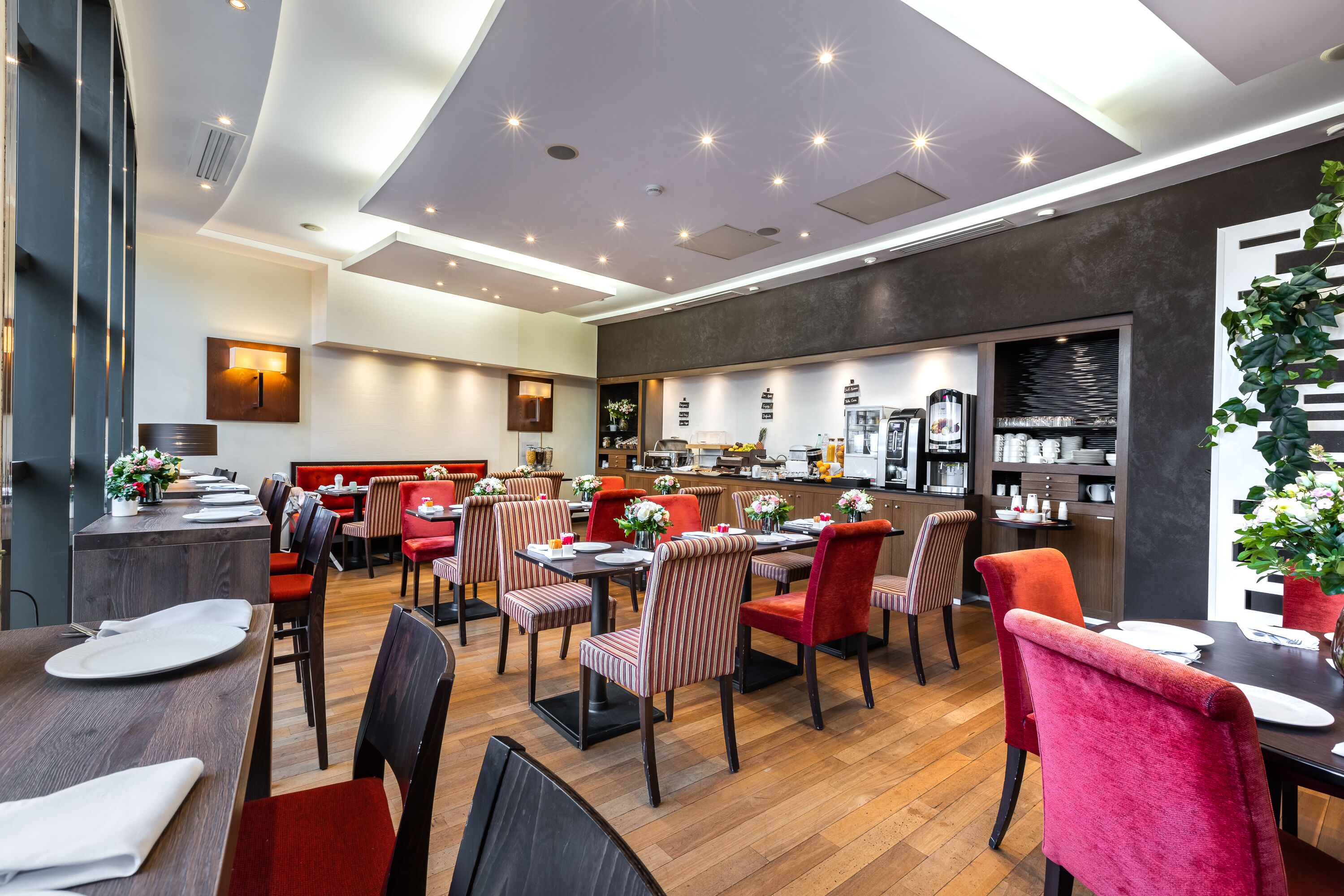 A modern restaurant with wooden flooring, red and striped chairs, and a kitchen area in the background.