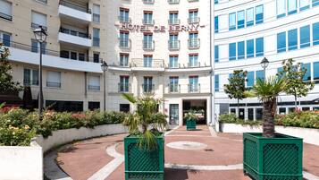A hotel entrance with a curved driveway, a palm tree, and a flower bed.