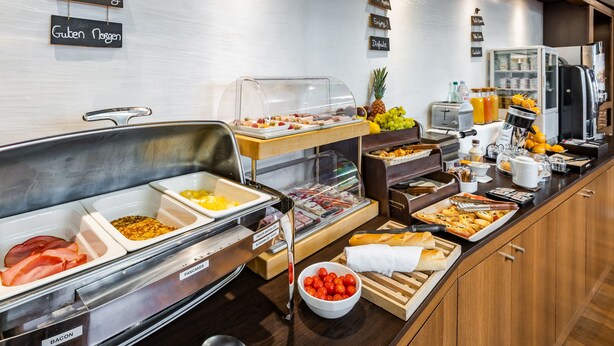 A buffet with labeled food sections including bacon, eggs, and various fruits. - Hôtel de Berny (Antony)