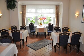 A dining area with tables set for four, chairs with dark upholstery, a patterned rug, and a view of the outdoors through large windows. - Bremer Apartmenthotel (Bremen)
