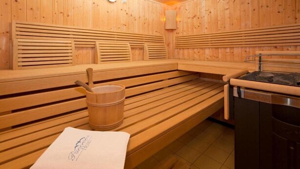 A sauna with wooden benches, a wooden bucket, and a towel on the bench. - Panoramahotel (Sankt Johann in Tirol)