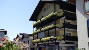 A multi-story hotel with balconies adorned with flowers, a visible sign for 'Marionnaud', and a street view with other buildings. - Panoramahotel (Sankt Johann in Tirol)