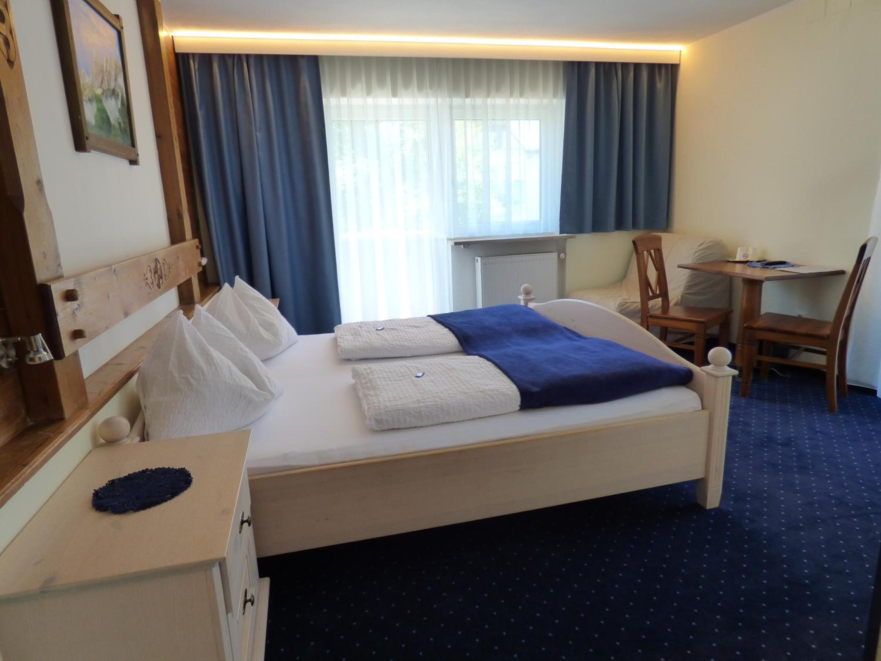 Una habitació d'hotel amb un llit, una escriptori, una cadira i una finestra amb cortines.