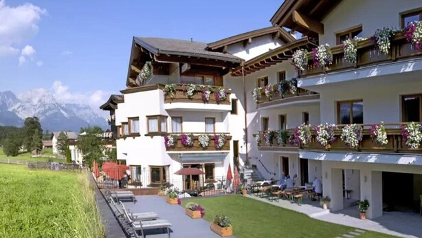 A multi-story hotel with balconies adorned with flowers, outdoor seating, and a view of mountains. - Ferienhotel Fuchs (Soell)