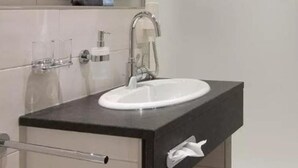 A bathroom with a white sink, black countertop, and a towel dispenser. - Ferienhotel Fuchs (Soell)