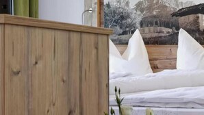 A wooden headboard, a bed with white bedding, and a mountain landscape painting in the background. - Ferienhotel Fuchs (Soell)