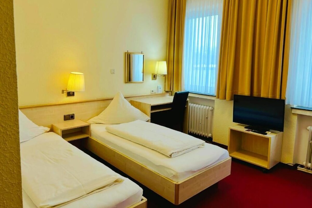 A hotel room with two beds, a desk, a chair, a TV, and a window with curtains.