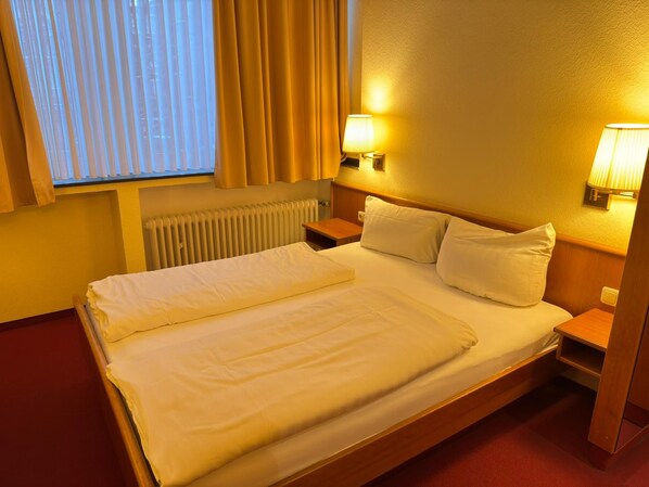 Een hotelkamer met een bed, nachtkastje, lamp en een raam met gordijnen.