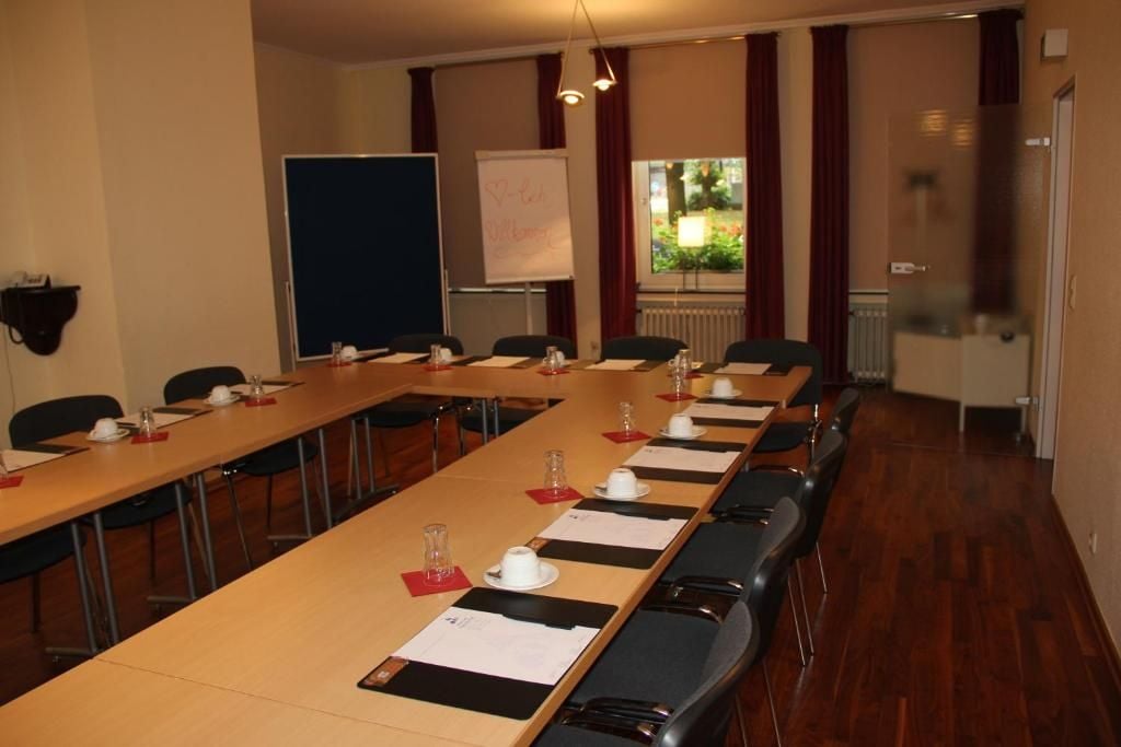 Une salle de conférence avec de longues tables, des chaises, un tableau blanc et une fenêtre avec des rideaux.