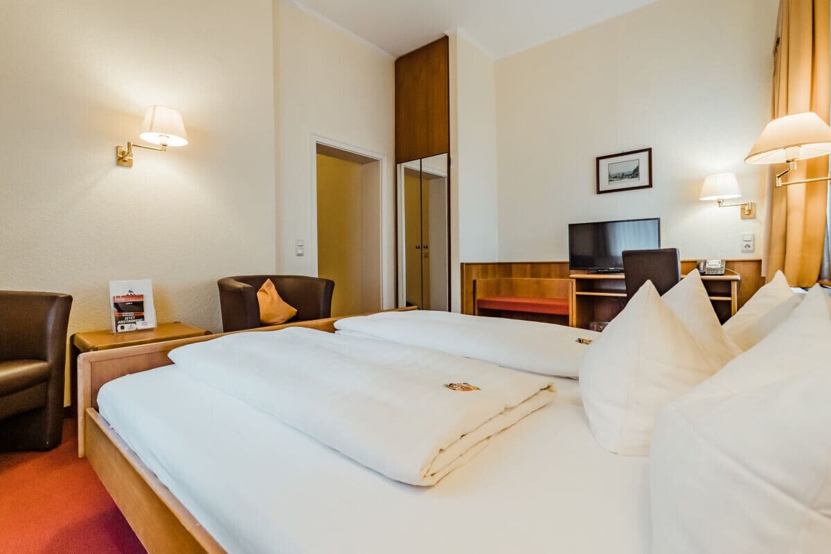 A hotel room with a large bed, a desk with a chair, a television, and a desk lamp.